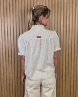 Camisa de manga corta color beige, con cuello alto con volados, botonadura frontal y mangas abullonadas con terminación fruncida.
