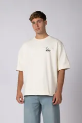 Remera de corte oversize color crudo, con cuello redondo y mangas cortas. Presenta un pequeño estampado gráfico en el pecho con diseño de aves en vuelo.
