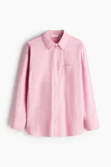 Camisa oversized a rayas color rosado y blanco, con cuello clásico, cierre frontal de botones, un bolsillo aplicado en el pecho y mangas largas con puños abotonados.