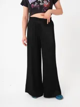 Pantalón negro de tiro alto, pierna ancha y silueta suelta, confeccionado en tejido con textura plisada o arrugada.