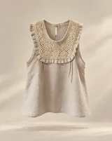 Blusa sin mangas de lino color beige, con pechera artesanal bordada con motivos florales y ribete de volados alrededor del escote y los hombros.