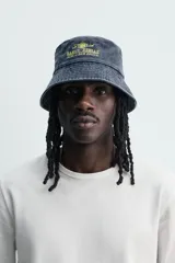 Sombrero tipo bucket de algodón con efecto lavado, color azul oscuro, con bordado frontal en tono amarillo que incluye la inscripción "Early Reggae Rub-A-Dub Sound". Cuenta con ala ancha con pespuntes decorativos.