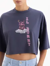 Remera blanca de corte cropped y manga corta, confeccionada en algodón. Presenta una estampa frontal con un conejo con estampado animal print sobre una nube y el texto 'IL BUNNY' en color amarillo.