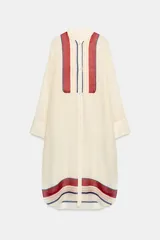 Vestido túnica semitransparente de cuello redondo y manga larga, de color crudo con detalles de rayas rojas, azules y beige en el pecho y el bajo. Cuenta con aberturas laterales y cierre frontal con botones.