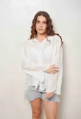 Camisa blanca de manga larga con bordados florales y detalles de ojales, cuello camisero y cierre frontal con botones ocultos.