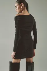 Vestido corto entallado de punto elástico, con diseño asimétrico de un solo hombro y manga larga. Presenta una capa superior drapeada y costuras fruncidas laterales que crean un efecto de pliegues en toda la prenda.