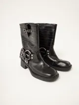 Botas de caña media estilo biker, confeccionadas en cuero vacuno con textura grabada. Presentan punta cuadrada, taco cuadrado de 5 cm y múltiples detalles metálicos, incluyendo hebillas ajustables y apliques circulares laterales.