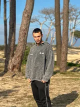 Canguro gris gastado con capucha, de calce relajado y diseño con estampado vertical en la espalda con el texto "la ola BOARD BRAND COMMUNITY surf skim skate".