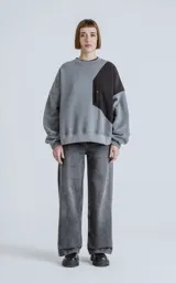 Buzo de cuello redondo con diseño oversize y corte crop. Confeccionado en frisa de algodón color gris melange, presenta un recorte asimétrico en color negro en microfibra con un bolsillo frontal funcional con cierre a presión.