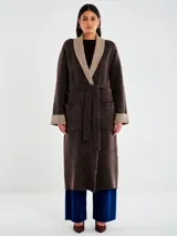 Saco largo de tejido de punto marrón oscuro con micro lentejuelas sutiles. Presenta un cuello chal ancho en color beige/tostado, puños doblados a tono y bolsillos aplicados. Se ajusta con un lazo o faja del mismo tejido principal.