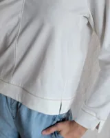 Remera de algodón color blanco, con escote en V y detalle de pespuntes decorativos en color beige. Presenta mangas largas y un corte recto con aberturas laterales en el ruedo.