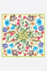 Chal cuadrado confeccionado en modal con un diseño de estampado botánico floral en tonos azul, fucsia, amarillo y naranja sobre un fondo crema. Presenta bordes en color verde con acabado deshilachado.