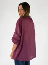 Blusa de manga larga color marrón, con cierre frontal de botones, escote en V y detalles de volados fruncidos alrededor del cuello y los puños elásticos.