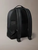 Mochila Calvin Klein de poliuretano color negro, de diseño minimalista con silueta redondeada. Cuenta con un compartimento principal con cierre, bolsillo frontal externo con cierre y el monograma CK grabado. Incluye asa superior y correas acolchadas ajustables.