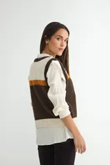 Chaleco tejido de punto con diseño de bloques de color en tonos marrón, naranja y crema. Presenta cuello redondo, cierre frontal con botones y terminaciones acanaladas en el ruedo y sisas.