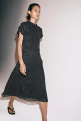 Vestido midi de viscosa con estampado de lunares blancos sobre fondo negro. Presenta cuello redondo con detalle de lazada, manga corta y pliegues en la cintura con bajo recto.