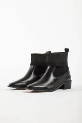 Bota de caña media combinada, con puntera y talón en cuero negro y caña de tejido de punto acanalado elástico. Cuenta con taco cuadrado bajo y tirador trasero.