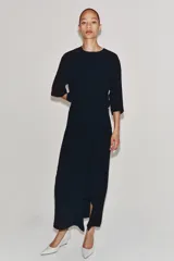Vestido midi de cuello redondo y manga corta, confeccionado en tejido fluido color azul marino. Presenta un diseño con detalle de drapeado y volado lateral en la parte delantera, con cierre en la espalda mediante abertura y botón.