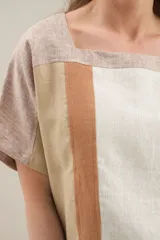 Blusa de lino de diseño contemporáneo, con escote cuadrado y mangas cortas en recortes que combinan distintas texturas. Su propuesta incorpora una franja vertical en contraste que aporta dinamismo y personalidad, mientras que el calce relajado la convierte en una prenda fresca y versátil.