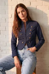 Chaqueta corta color beige de algodón, de inspiración militar con cuello mao y doble botonadura frontal con botones metálicos dorados.