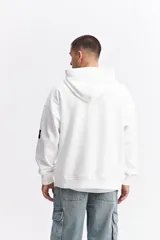 Canguro oversize color marrón, con capucha, cordones ajustables, bolsillo frontal con cierre y estampa frontal con texto y logo de la marca.