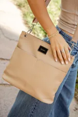 Bandolera color beige de cuero sintético con correa ancha de tela ajustable. Tiene dos bolsillos frontales y cierre metálico.