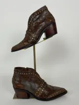 Botas cortas de cuero color chocolate con acabado desgastado y detalle de tachas metálicas. Presentan un taco cuadrado de madera y punta fina.