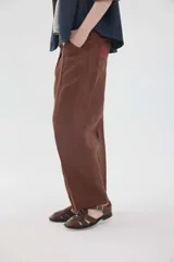 Pantalón de lino marrón de tiro medio, con calce holgado y diseño de piernas amplias. Cuenta con bolsillos traseros, trabillas para cinto y un pin bordado en contraste.