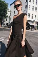 Vestido midi negro con escote asimétrico de un solo hombro, cuerpo ajustado y falda amplia de corte asimétrico con frunces en la cintura.