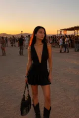 Vestido corto negro con escote profundo en V, sin mangas y falda con volados. Presenta un diseño ajustado en la cintura con detalle drapeado.