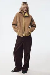 Chaqueta de punto de textura bouclé en color marrón, con cuello subido, manga larga y cierre frontal con cremallera. Presenta detalles de ribetes y acabados en color verde lima a contraste en cuello, cierre, bolsillos y puños.