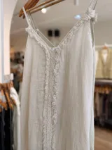 Vestido maxi de lino color blanco, con escote en V, tirantes finos regulables y detalles de flecos en el frente.