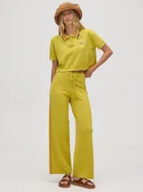 Pantalón de punto color verde oliva, confeccionado en algodón, con corte holgado, pierna ancha y tiro alto. Cuenta con pretina elástica con cordón de ajuste y una línea lateral a contratono en color naranja.
