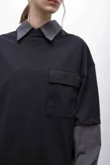 Remerón negro con cuello camisero, mangas largas con puños elásticos y bolsillo con solapa en el pecho.