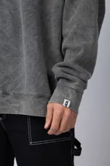 Buzo de cuello redondo y corte oversize, confeccionado en tela friza con efecto de teñido artesanal desgastado. Presenta un estampado pequeño en color verde lima en el pecho y una etiqueta pequeña en el puño.