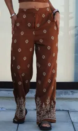 Conjunto de dos piezas compuesto por un top corto tipo strapless y un pantalón de corte holgado, ambos en color marrón con estampado geométrico étnico. El pantalón presenta un diseño de pierna ancha con detalle de guarda decorativa en el ruedo.