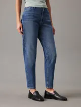 Pantalón de jean azul de corte mom, tiro alto, pierna recta y tobillo ajustado. Confeccionado con denim comfort stretch de peso medio, con un 20% de algodón reciclado. Cuenta con bragueta con cremallera, diseño de cinco bolsillos, herrajes de Calvin Klein e insignia de Piel.
