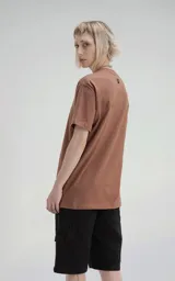 Remera de manga corta y cuello redondo, color marrón (mocca), confeccionada en algodón premium suave. Presenta un calce regular con un recorte distintivo en la espalda.