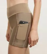 Bermuda deportiva femenina de corte ajustado, color marrón claro con acabado satinado. Presenta pretina ancha y tiro alto.