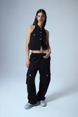 Chaleco de denim negro con escote halter y cuello camisero. Se abrocha al frente con botones metálicos con el logo grabado. Presenta dos bolsillos con tapa en el pecho y espalda descubierta.