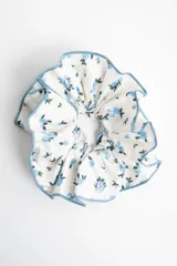 Gomita para el pelo de diseño voluminoso, con estampado floral en tonos celestes sobre fondo blanco y terminación de ruloté celeste en los bordes.