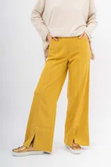 Pantalón ancho de color mostaza con costuras contrastantes en blanco. Presenta un corte recto y aberturas en los bajos delanteros.