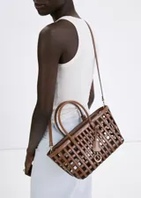 Bolso tipo cesta de color marrón, con diseño trenzado y estructura cuadriculada, asas cortas de mano y correa larga ajustable y desmontable. Incluye charm decorativo y cierre de cremallera.