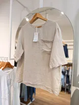 Blusa de lino color beige, de corte relajado, con escote redondo, mangas amplias y bolsillo delantero con detalle de lentejuelas.