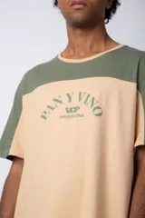 Remera de algodón con diseño color block, combinando tonos beige y verde militar. Presenta cuello redondo y estampa frontal con la frase 'Pan y Vino' y el logo 'VCP Argentina'.