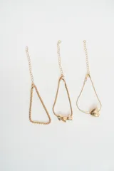 Set de tres pulseras doradas de cadena fina con cierre de mosquetón y cadena de alargue. Incluye una pulsera de cadena trenzada, una pulsera de cadena tipo serpiente con tres dijes de corazones pequeños y una pulsera de cadena tipo serpiente con un dije de corazón grande texturizado.