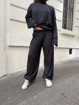 Conjunto de dos piezas compuesto por un buzo de cuello alto y mangas largas con diseño holgado, y un pantalón a juego. Ambas prendas están confeccionadas en tejido morley elastizado de color negro con un sutil efecto jaspeado.