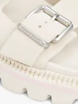 Sandalias planas de color blanco hueso con dos tiras ajustables mediante hebillas metálicas. Cuentan con una suela gruesa y dentada de plataforma.