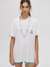 Remera de corte cuadrado y ajuste holgado, color verde oliva, con pequeño estampado gráfico de un velero en el pecho y etiqueta decorativa en la manga.