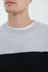 Sweater deportivo de hombre con escote redondo, diseño colorblock con la parte superior en gris claro y el cuerpo y mangas en negro. Presenta puños y cintura elastizados.